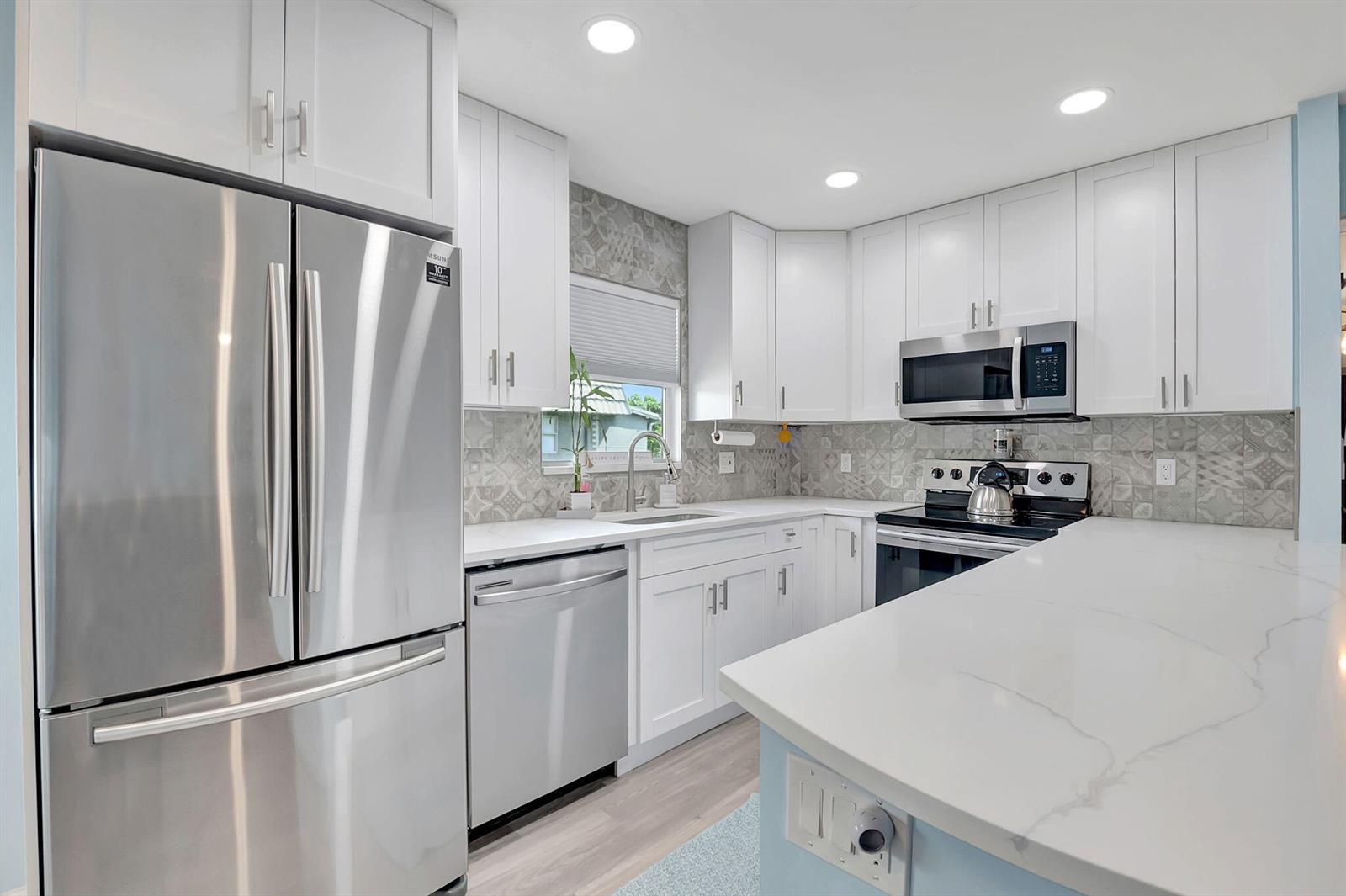 A modern kitchen features white cabinets, stainless steel appliances, and a patterned tile backsplash — 89 Flanders Way # B, Delray Beach FL 33484, DELRAY BEACH, FL