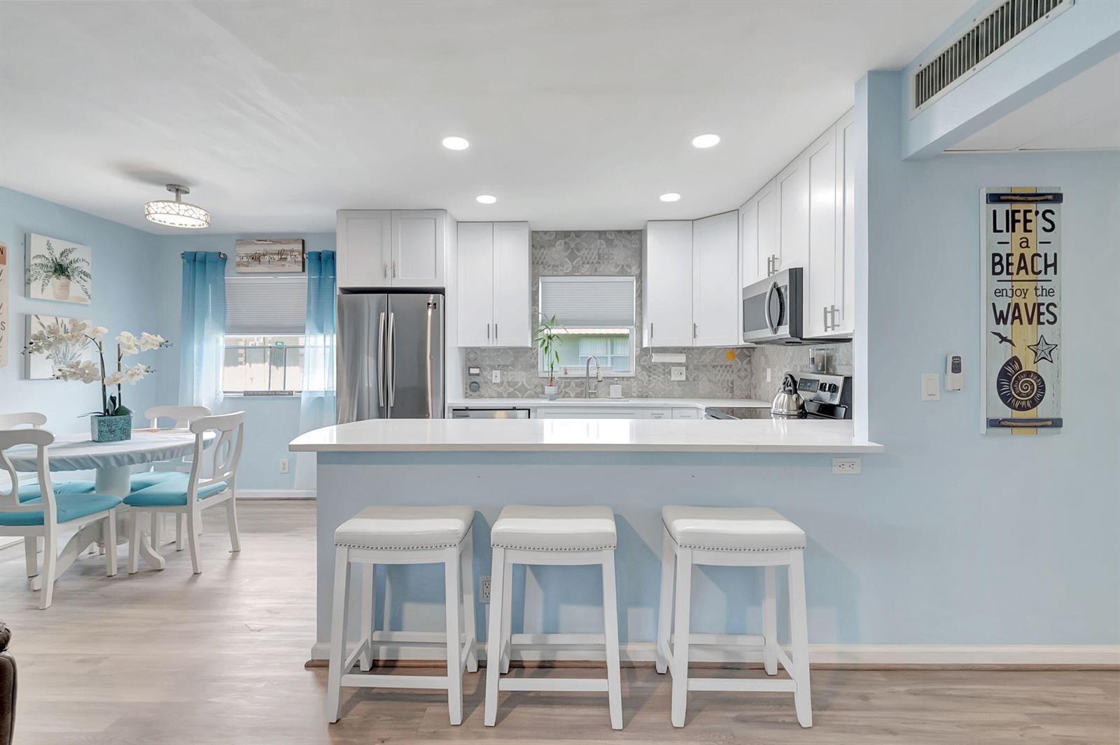 A kitchen with white cabinets, stainless steel appliances, and a breakfast bar with three stools — 89 Flanders Way # B, Delray Beach FL 33484, DELRAY BEACH, FL