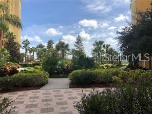 A paved walkway leads through a landscaped courtyard between two tall residential buildings — 8100 POINCIANA BOULEVARD UNIT 2106, ORLANDO, FL