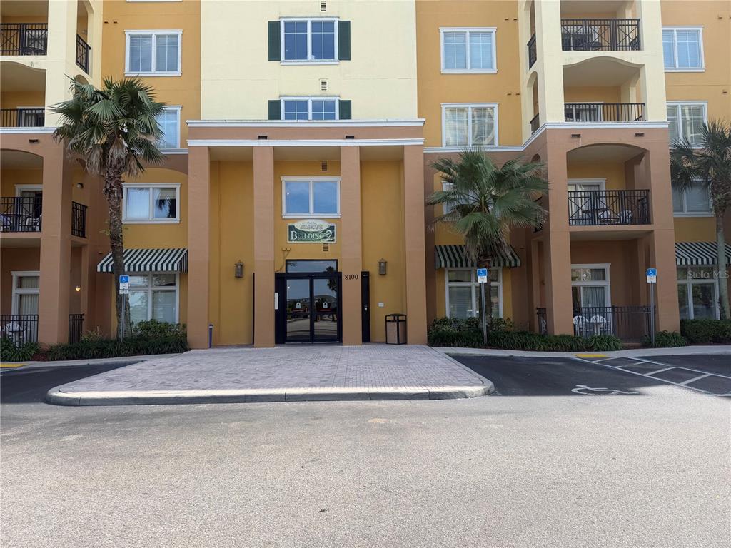 The exterior of a multi-story apartment building features a central entrance with a paved walkway — 8100 POINCIANA BOULEVARD UNIT 2106, ORLANDO, FL
