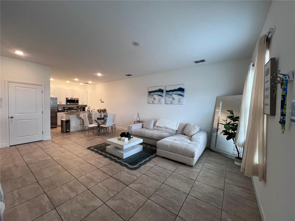 A living room with tile floors, a sectional sofa, and an open kitchen in the background — 1631 CUMIN DRIVE, KISSIMMEE, FL