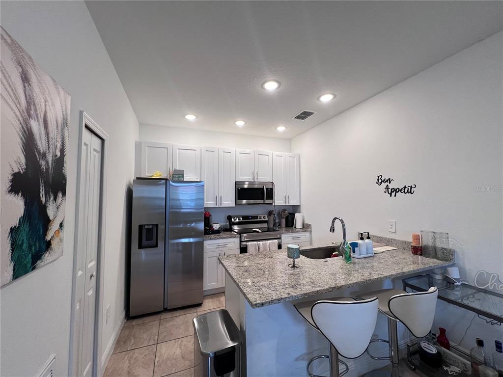 A kitchen features white cabinets, stainless steel appliances, granite countertops, and a breakfast bar — 1631 CUMIN DRIVE, KISSIMMEE, FL
