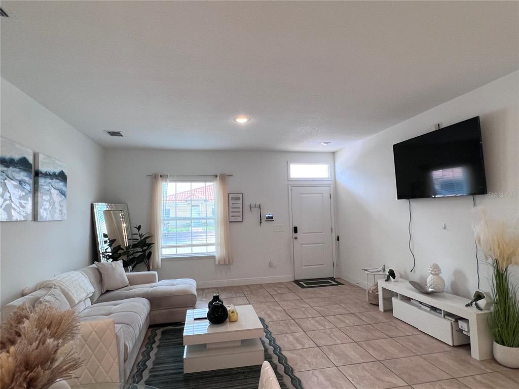 A living room features a sectional sofa, a coffee table, and a wall-mounted television — 1631 CUMIN DRIVE, KISSIMMEE, FL
