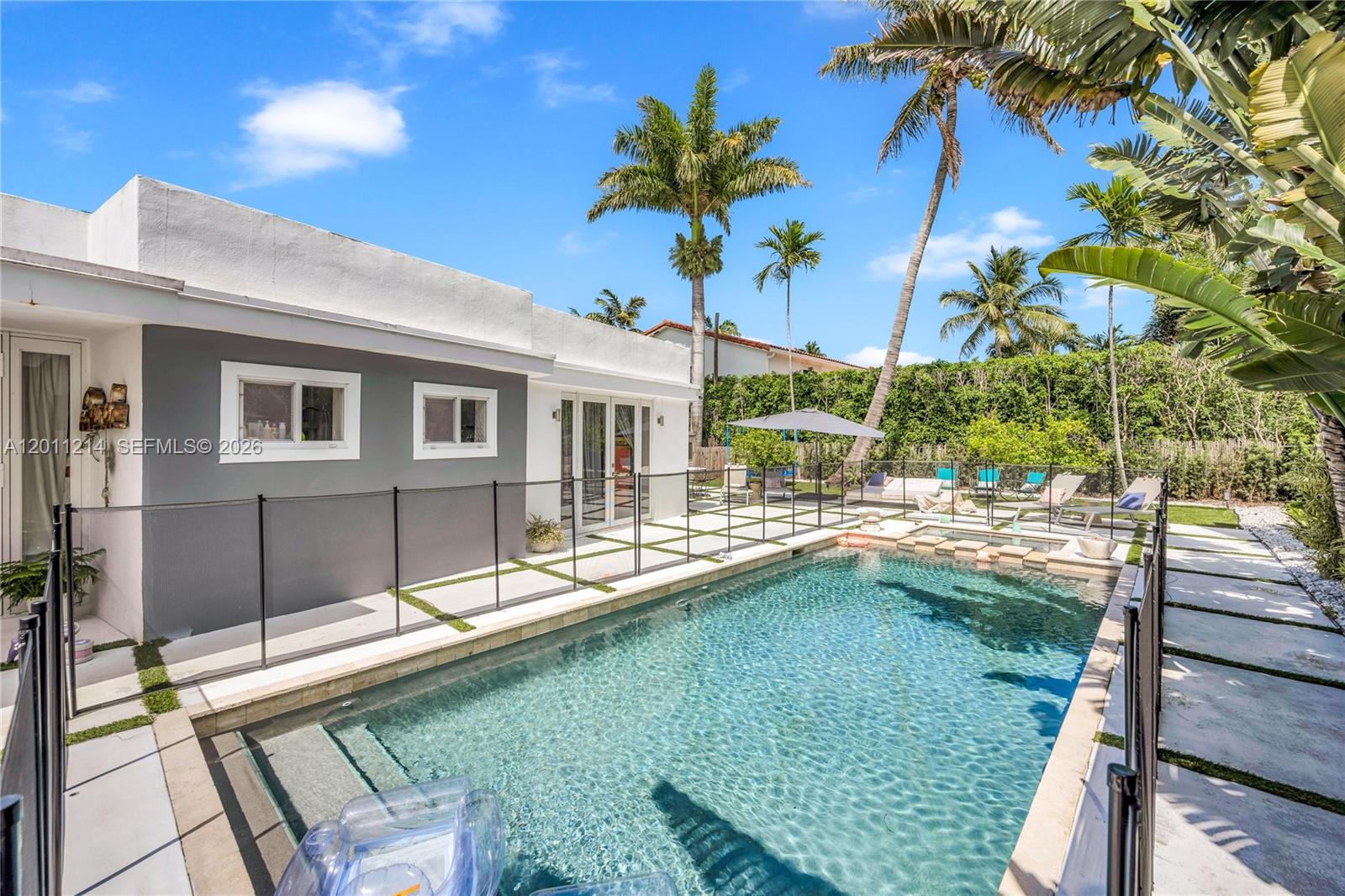 A swimming pool with a safety fence sits beside a house with a gray wall — 4975 Delaware Ave # 0, Miami Beach FL 33140, MIAMI BEACH, FL