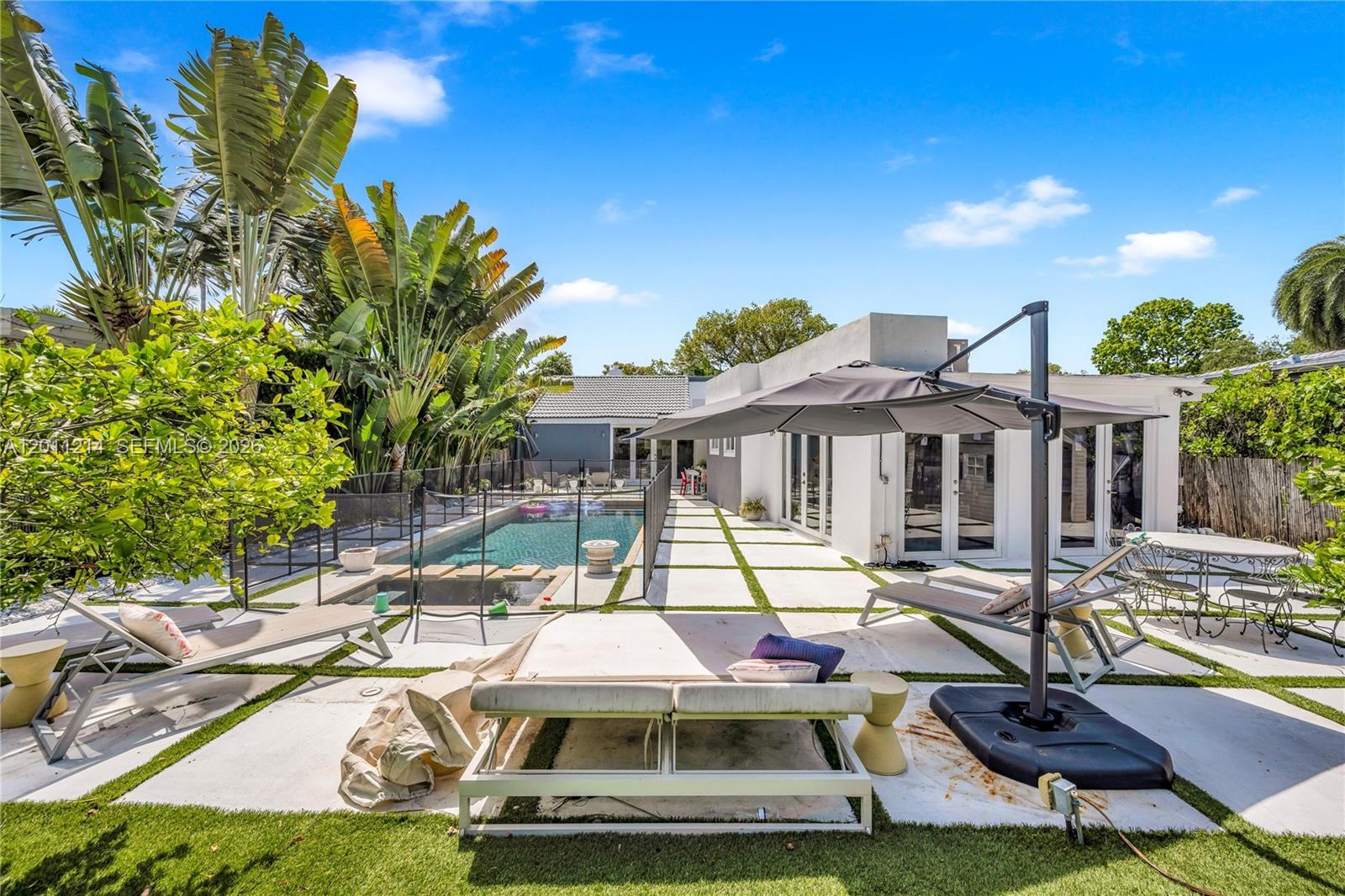 A backyard features a swimming pool, lounge chairs, a patio umbrella, and modern concrete pavers — 4975 Delaware Ave # 0, Miami Beach FL 33140, MIAMI BEACH, FL