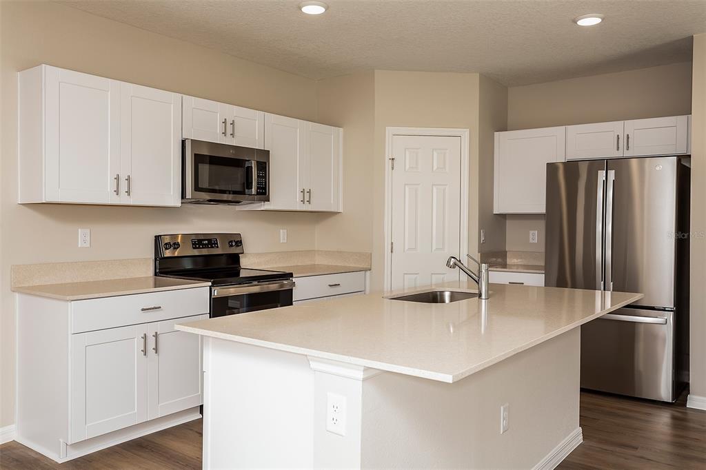 A kitchen features white cabinets, stainless steel appliances, and a central island with quartz countertops — 6051 PRAIRIE RUN, HAINES CITY, FL