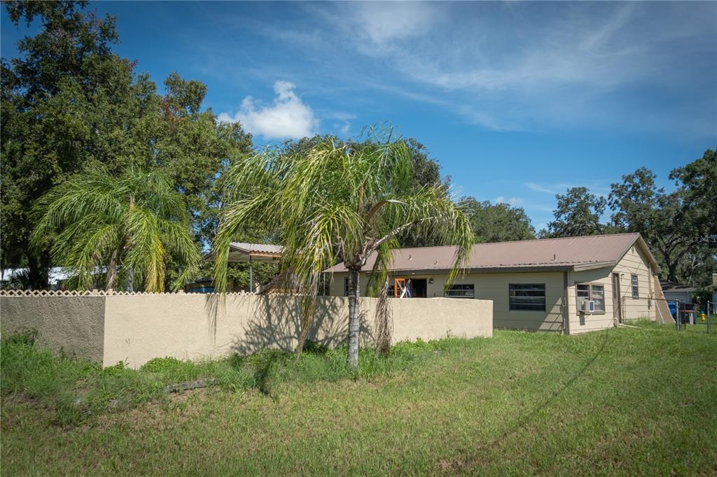 A single-story house with a metal roof and a tan stucco wall in the yard — 11013 MARIAN LANE, RIVERVIEW, FL