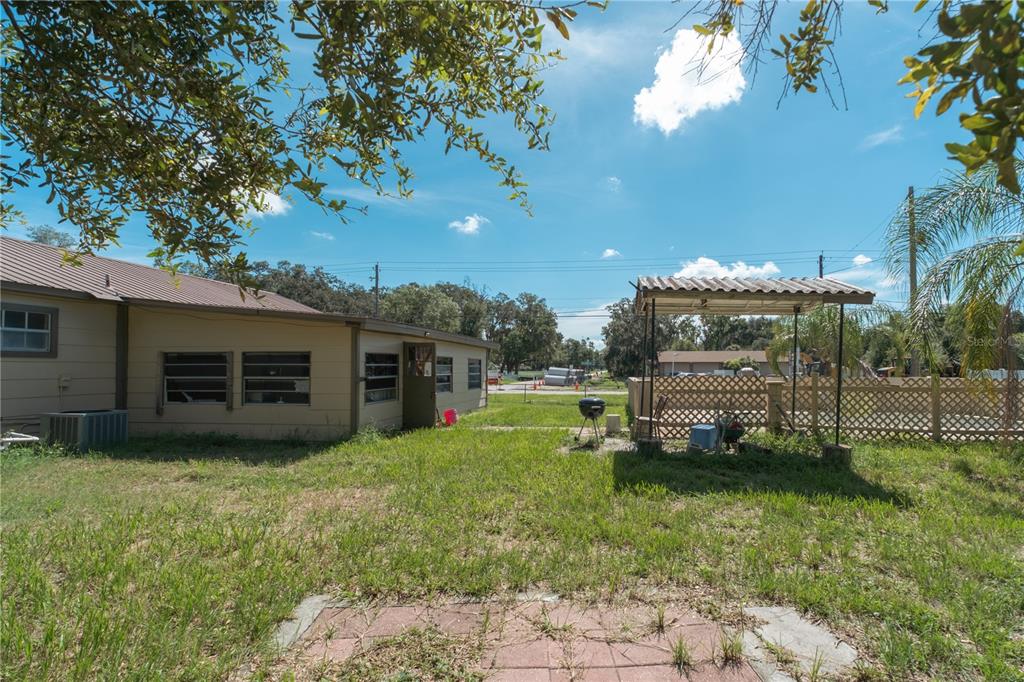 A backyard view featuring a tan house, a small covered patio, and a wooden fence — 11013 MARIAN LANE, RIVERVIEW, FL