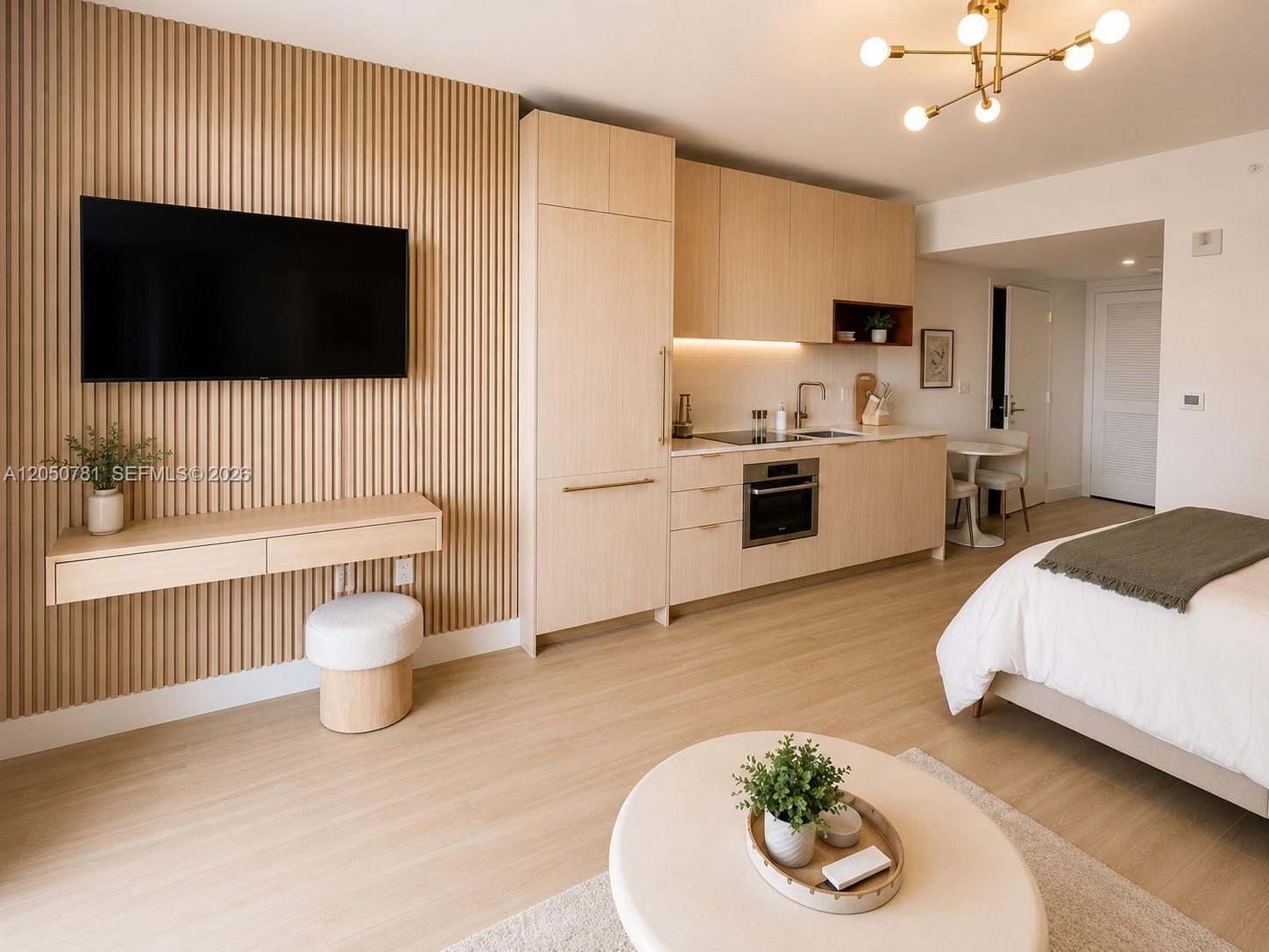 A studio apartment features light wood cabinetry, a slatted accent wall, and a mounted television — 90 NE 32 # 713, Miami FL 33137, MIAMI, FL