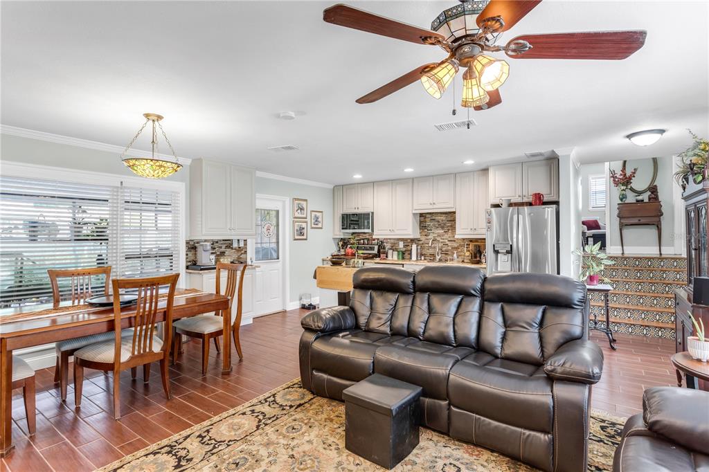 An open-concept living and dining area features wood-look tile flooring, a leather sofa, and cabinetry — 4508 S COOPER PLACE, TAMPA, FL