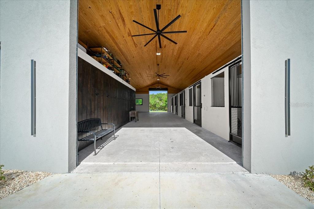 A modern horse stable aisle features a wood-paneled ceiling, concrete floors, and metal stalls — 3888 SW 140TH AVENUE, OCALA, FL