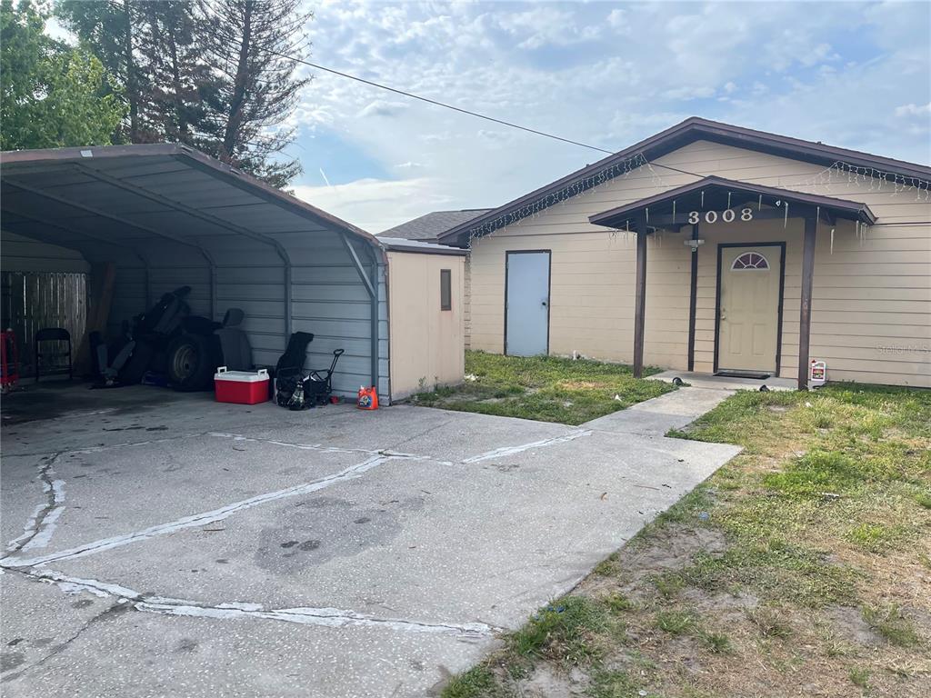 A beige house with a front porch and a metal carport on a concrete driveway — 3008 SKYVIEW DRIVE, LAKELAND, FL