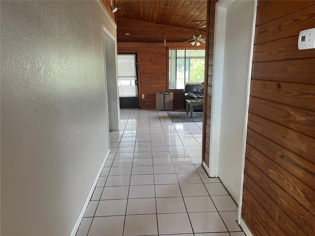 A hallway with white tile flooring leads to a living area with wood-paneled walls — 3008 SKYVIEW DRIVE, LAKELAND, FL
