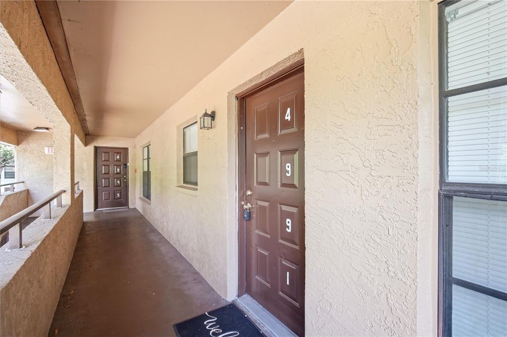 An exterior view of an apartment building hallway with brown doors and a concrete walkway — 4991 PURITAN CIRCLE UNIT 0522, TAMPA, FL
