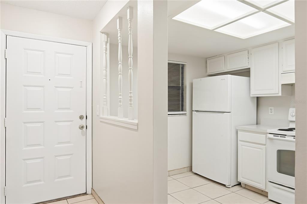 A white kitchen features a refrigerator, stove, and a pass-through window with decorative spindles — 4991 PURITAN CIRCLE UNIT 0522, TAMPA, FL