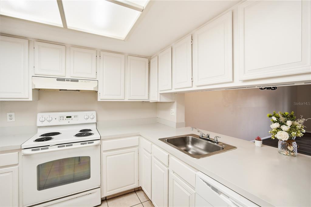A kitchen features white cabinets, white appliances, a stainless steel sink, and light countertops — 4991 PURITAN CIRCLE UNIT 0522, TAMPA, FL