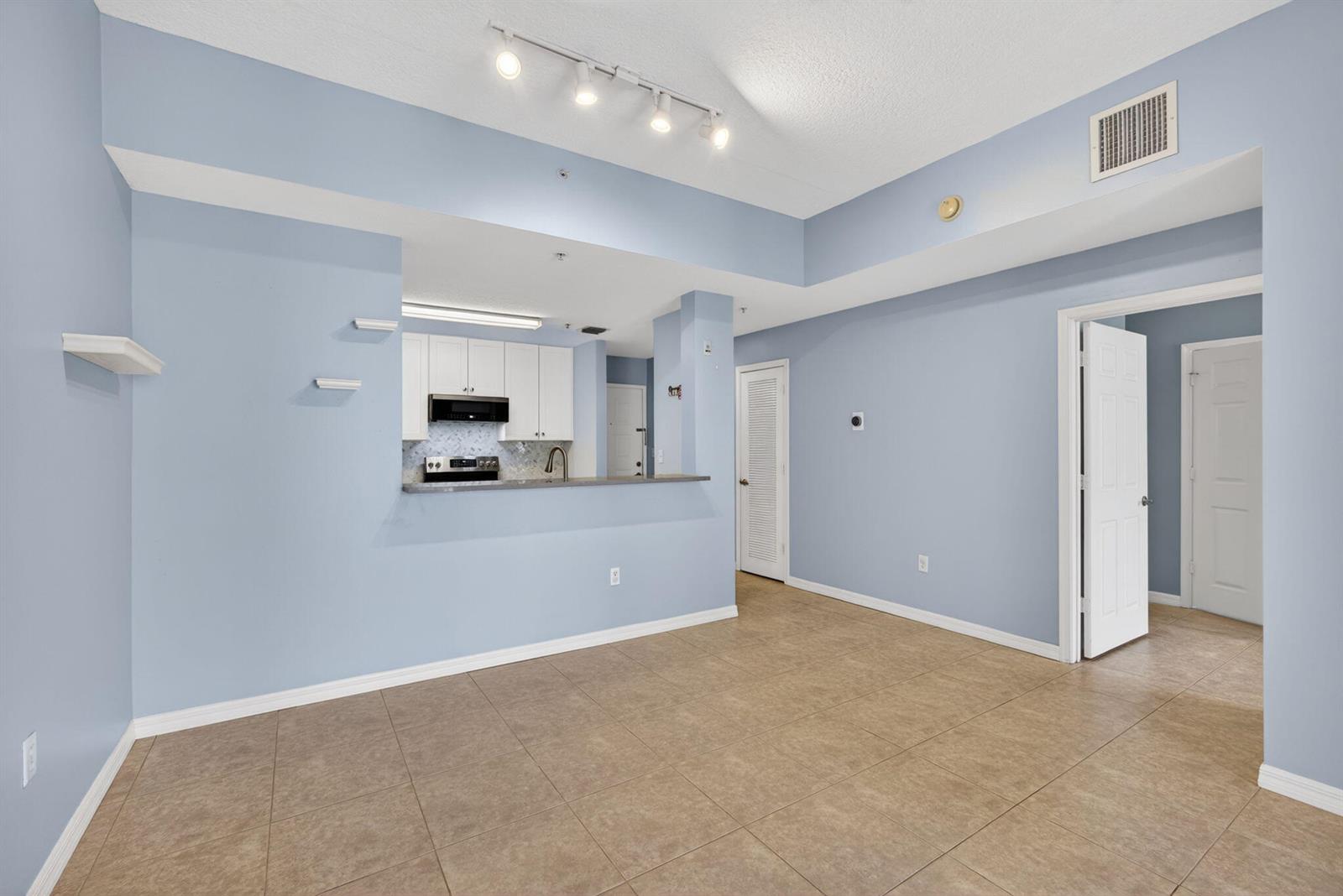 An empty room with light blue walls, tile flooring, and an open kitchen pass-through — 1203 Town Center Drive Drive # 308, Jupiter FL 33458, JUPITER, FL