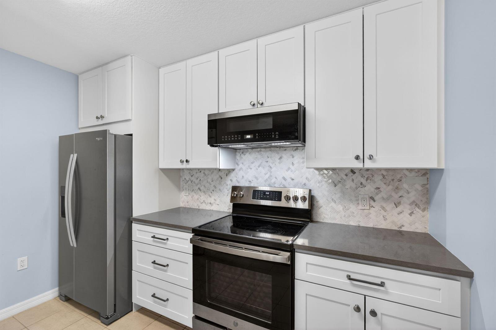 A kitchen features white cabinets, stainless steel appliances, dark countertops, and a herringbone tile backsplash — 1203 Town Center Drive Drive # 308, Jupiter FL 33458, JUPITER, FL