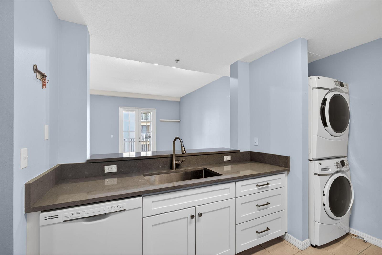 A kitchen features white cabinets, dark countertops, a sink, a dishwasher, and a stacked washer-dryer — 1203 Town Center Drive Drive # 308, Jupiter FL 33458, JUPITER, FL