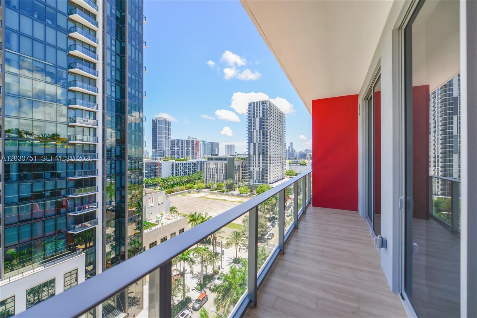 A balcony with wood-look flooring, a glass railing, and a vibrant red accent wall — 90 NE 32 St # 1108, Miami FL 33137, MIAMI, FL