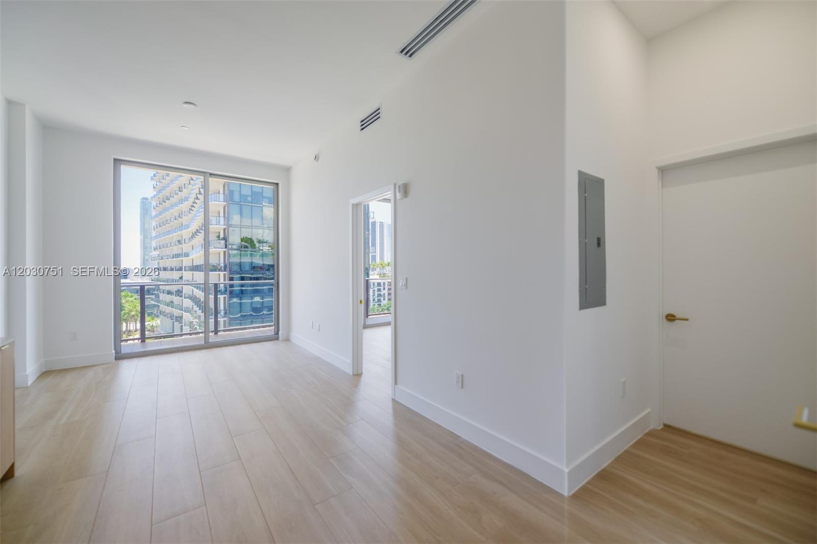 An empty room features light wood-look flooring, white walls, a doorway, and a glass balcony door — 90 NE 32 St # 1108, Miami FL 33137, MIAMI, FL