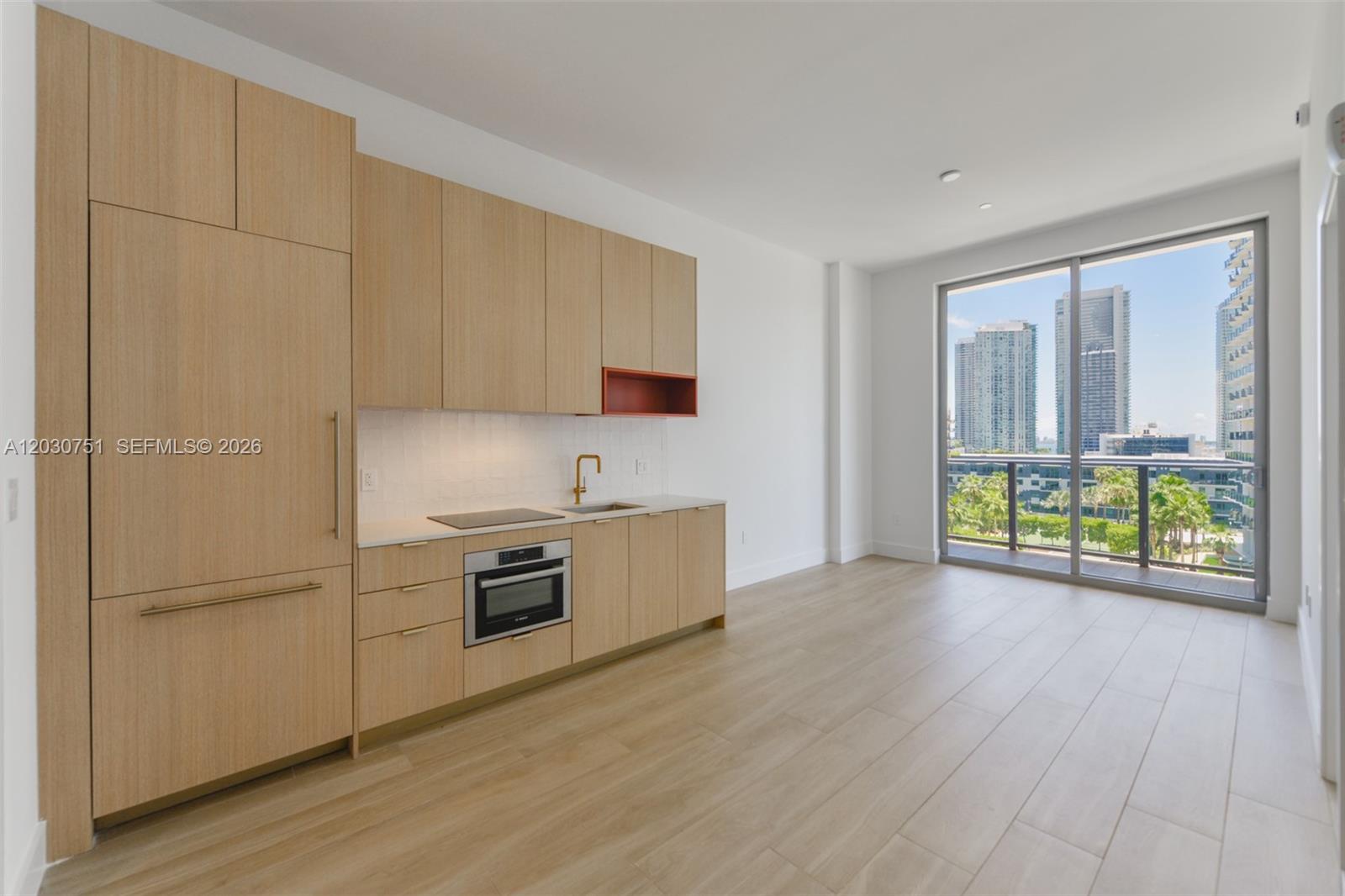 A modern kitchen with light wood cabinetry and a balcony overlooking city skyscrapers — 90 NE 32 St # 1108, Miami FL 33137, MIAMI, FL