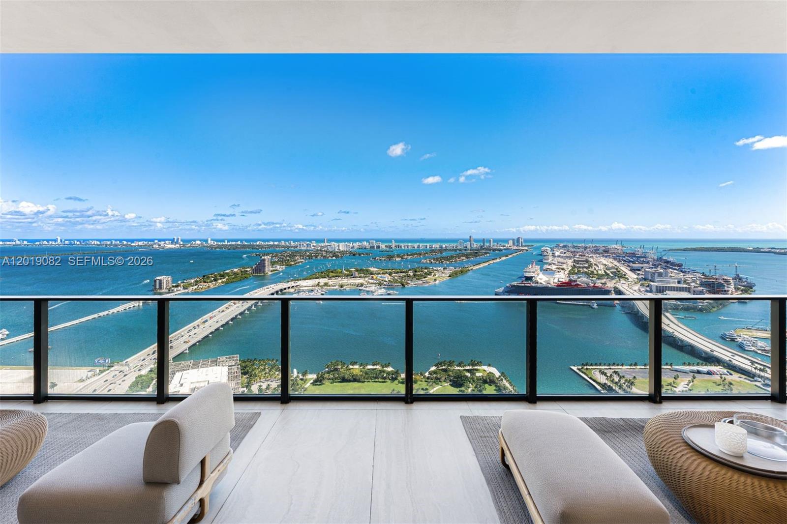 A balcony with modern seating overlooks a bay, a bridge, and a distant city skyline — 1000 Biscayne Blvd # 5101, Miami FL 33132, MIAMI, FL