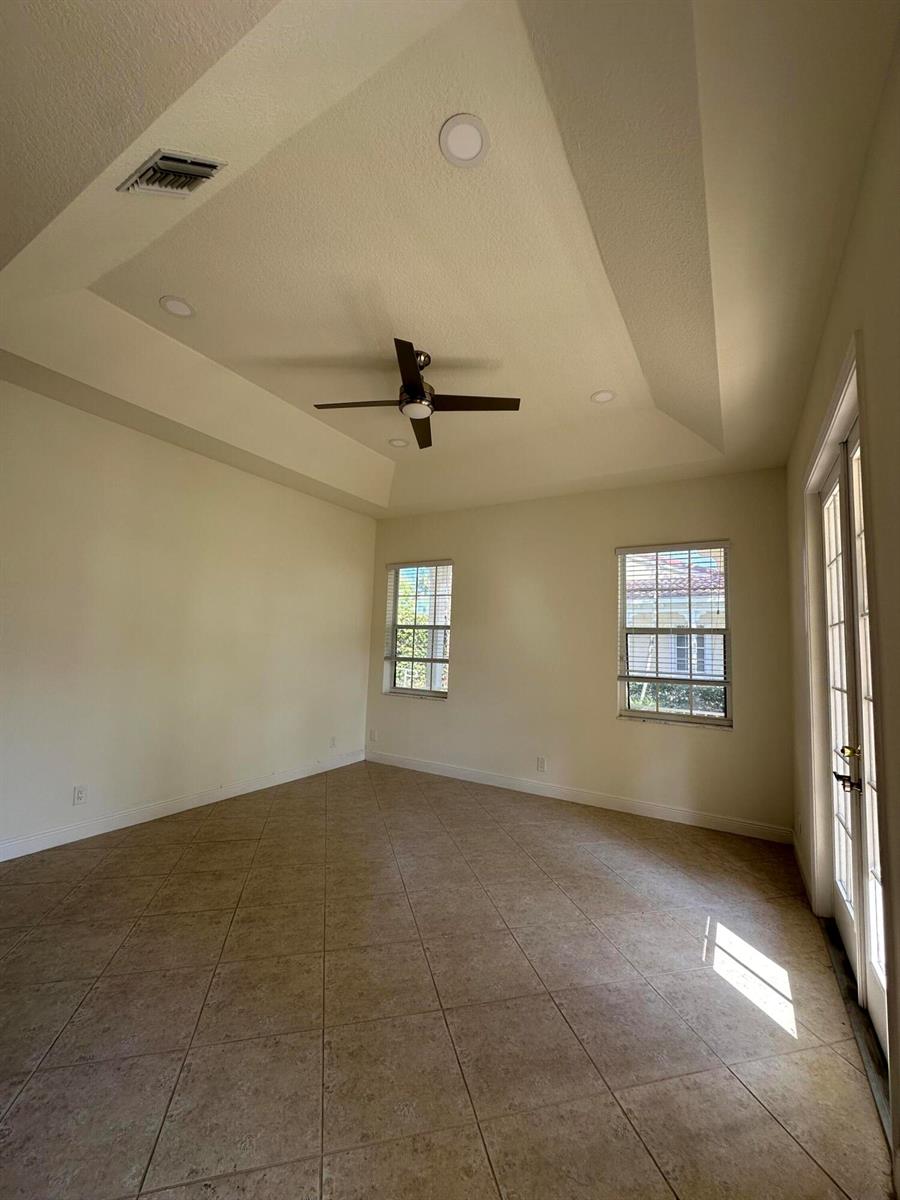 An empty room with tile flooring, a tray ceiling with a fan, and glass doors — 132 Mangrove Bay Way, Jupiter FL 33477, JUPITER, FL