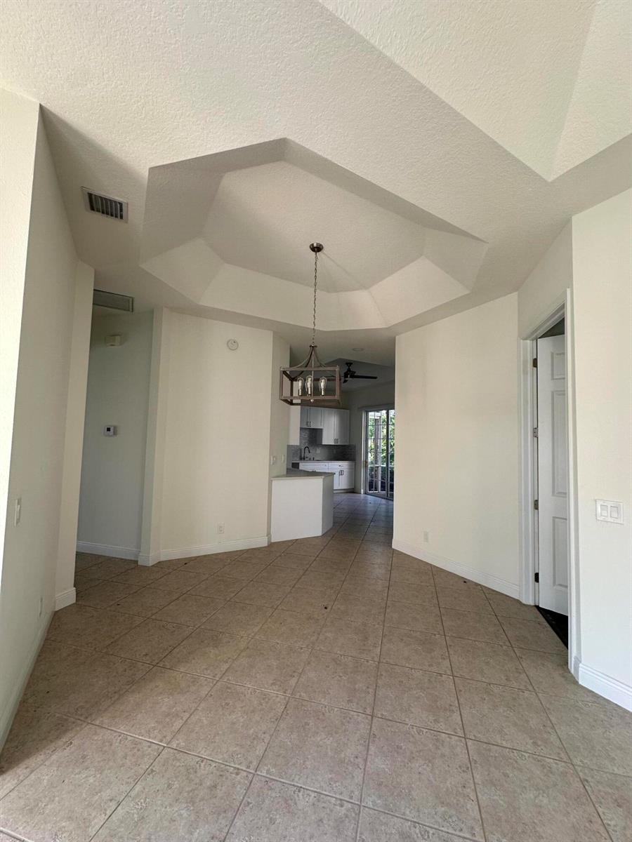 A dining area with a tray ceiling and chandelier leads to a kitchen with tile floors — 132 Mangrove Bay Way, Jupiter FL 33477, JUPITER, FL