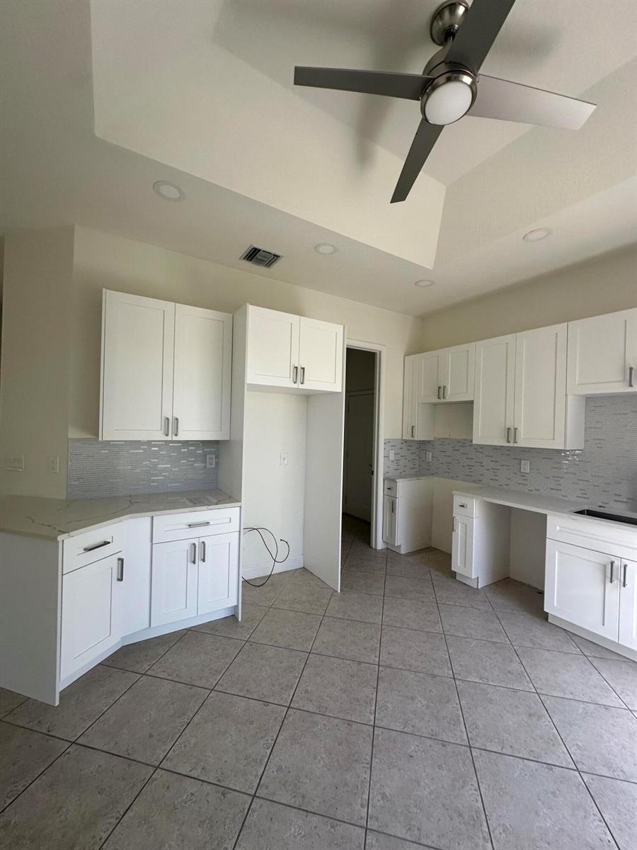 A kitchen features white cabinets, light countertops, a tiled backsplash, and a ceiling fan — 132 Mangrove Bay Way, Jupiter FL 33477, JUPITER, FL