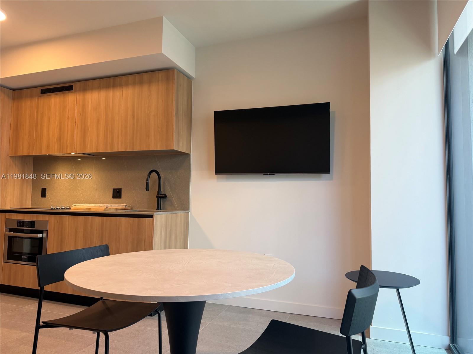 A modern kitchen with light wood cabinetry and a round dining table with black chairs — 121 NE 5Th ST # 912A, Miami FL 33132, MIAMI, FL