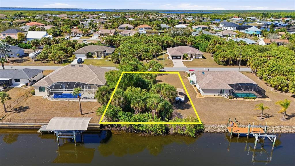 An aerial view shows a vacant, wooded waterfront lot situated between two residential houses — 4250 LIBRARY STREET, PORT CHARLOTTE, FL