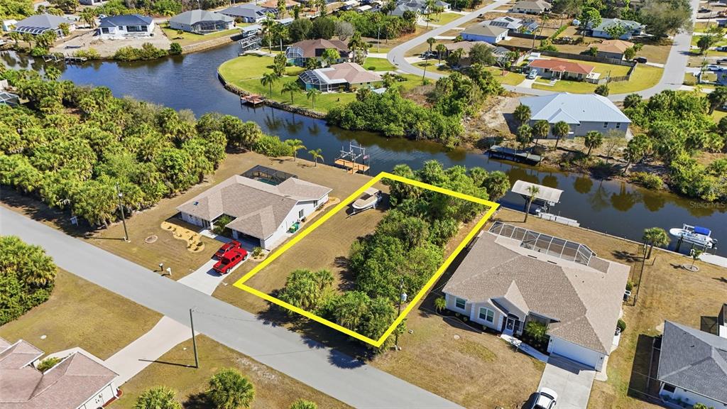 An aerial view shows a vacant, rectangular residential lot situated between two houses along a canal — 4250 LIBRARY STREET, PORT CHARLOTTE, FL