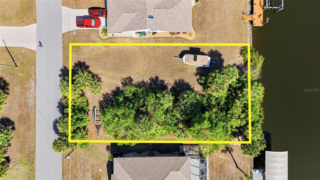 An aerial view shows a rectangular vacant waterfront lot bordered by trees and neighboring houses — 4250 LIBRARY STREET, PORT CHARLOTTE, FL