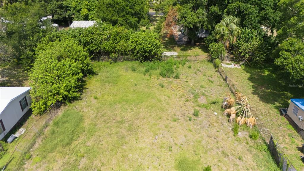 An aerial view shows a vacant, grassy rectangular lot bordered by trees and neighboring houses — 5013 DACCA DRIVE, TAMPA, FL