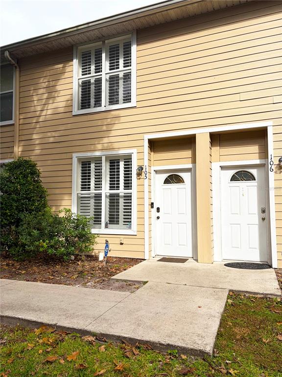A two-story townhouse exterior with tan siding, white trim, and two adjacent front doors — 3521 SW 30TH WAY UNIT 105, GAINESVILLE, FL