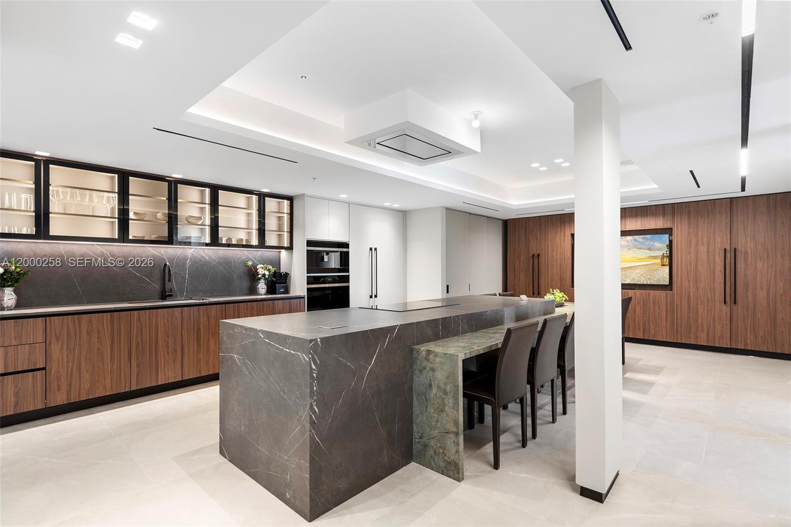 A modern kitchen features a large dark marble island, wood cabinetry, and integrated appliances — SUNNY ISLES BEACH, FL