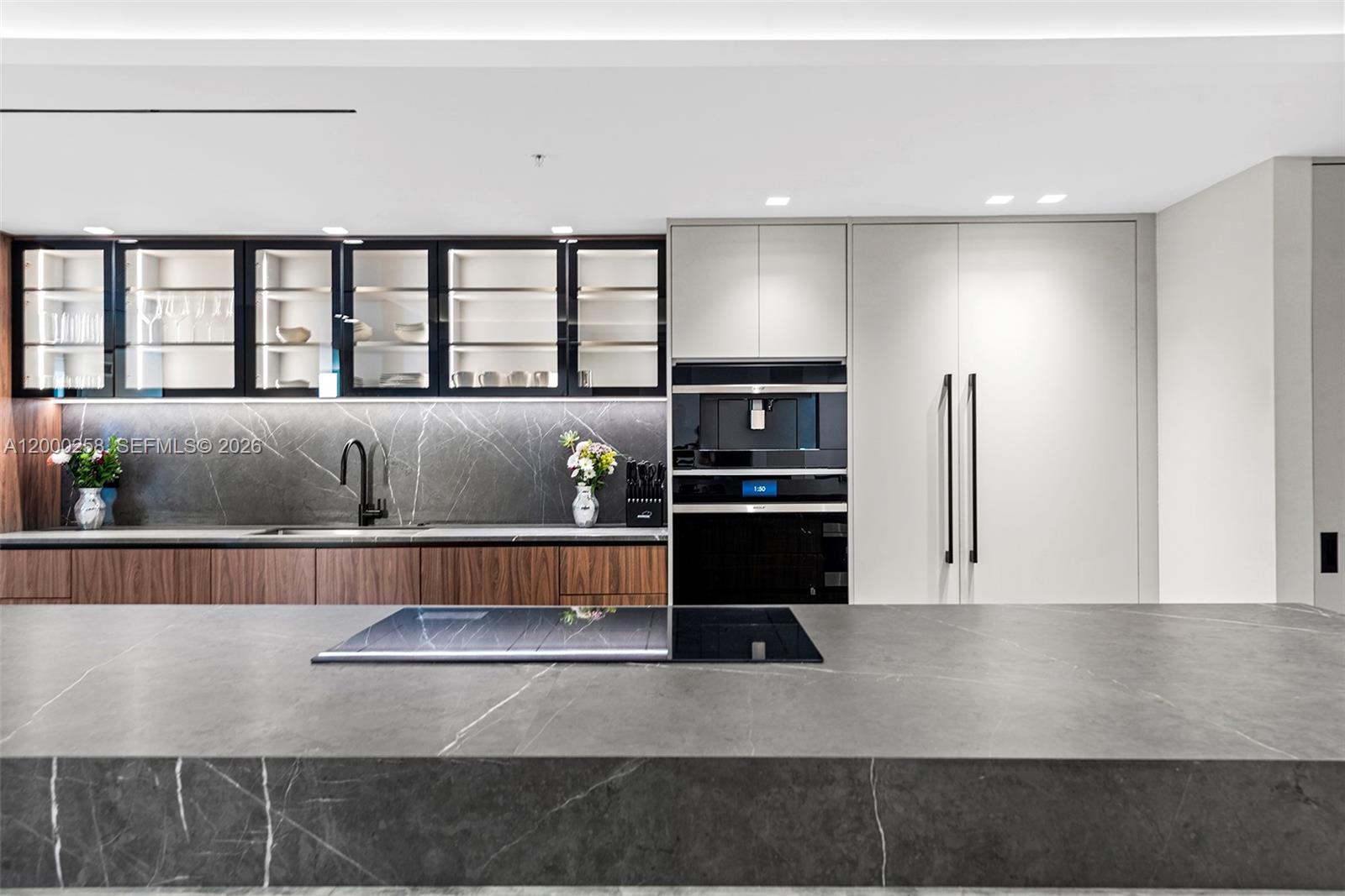A modern kitchen features a dark stone island, wood cabinetry, and integrated appliances — SUNNY ISLES BEACH, FL