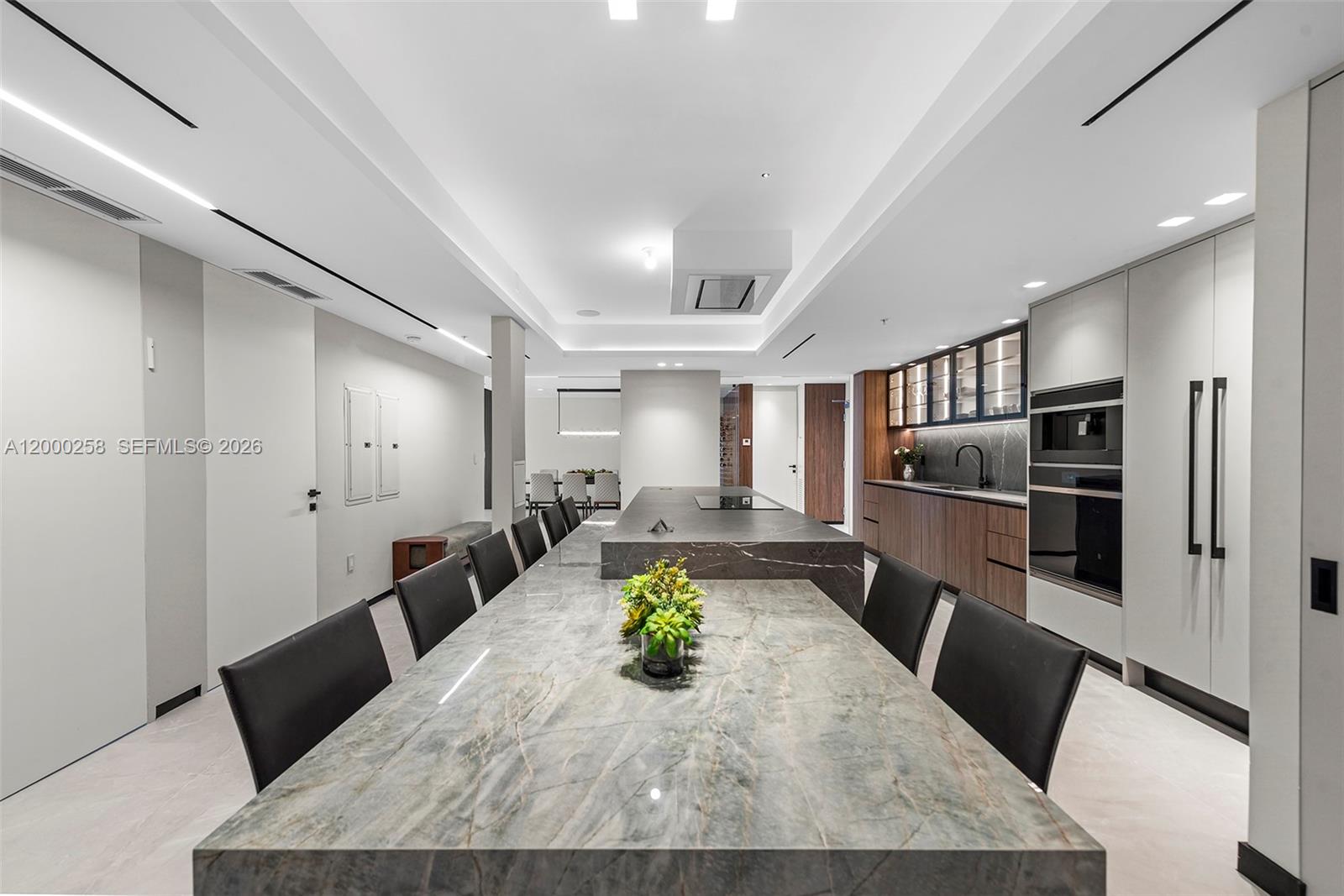 A modern kitchen features a long stone island with integrated seating and dark cabinetry — SUNNY ISLES BEACH, FL