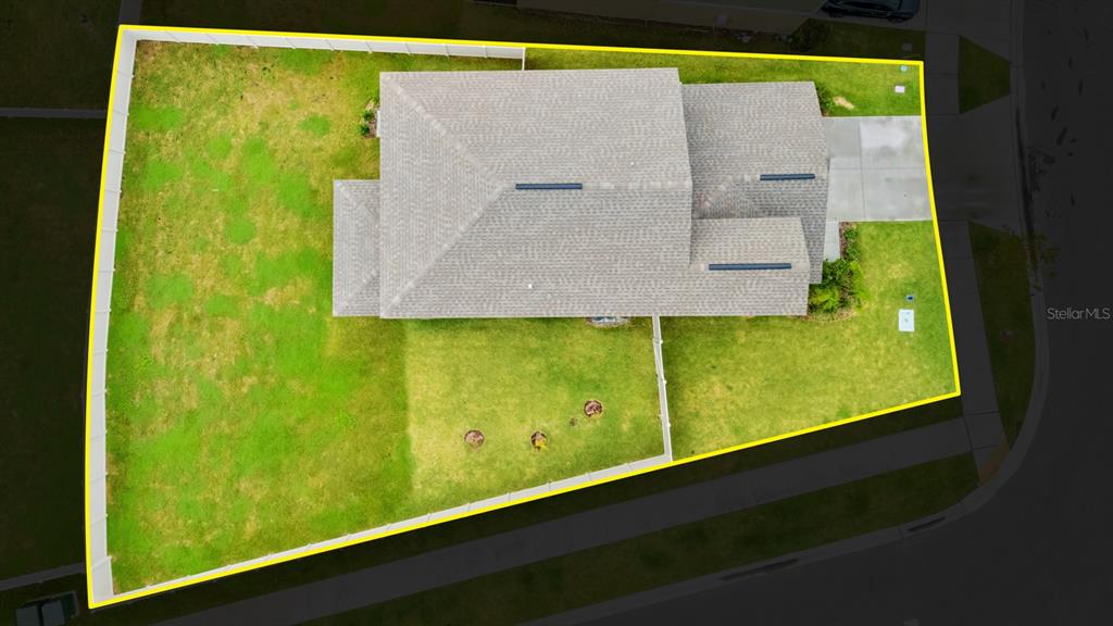 An aerial view shows a house with a gray roof situated on a fenced corner lot — 9520 RUNAWAY BREEZE, LAND O LAKES, FL