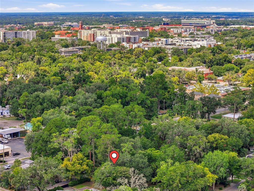 An aerial view shows a wooded lot marked with a pin near a city skyline — 616 NW 8TH PLACE, GAINESVILLE, FL