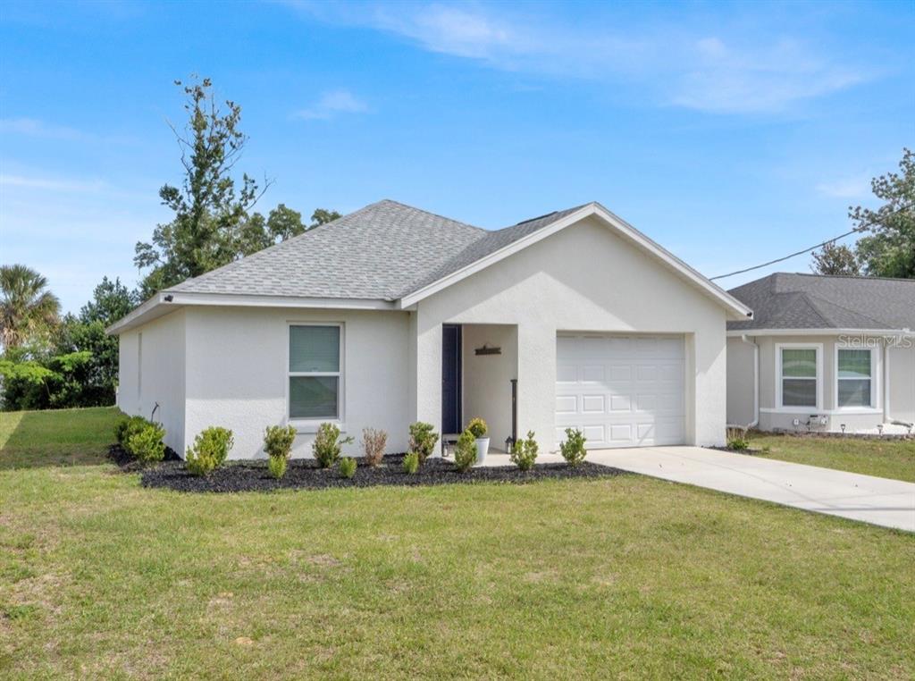 A living room with a gray sofa opens into a kitchen with white cabinets — 5311 SE 135TH PLACE, SUMMERFIELD, FL