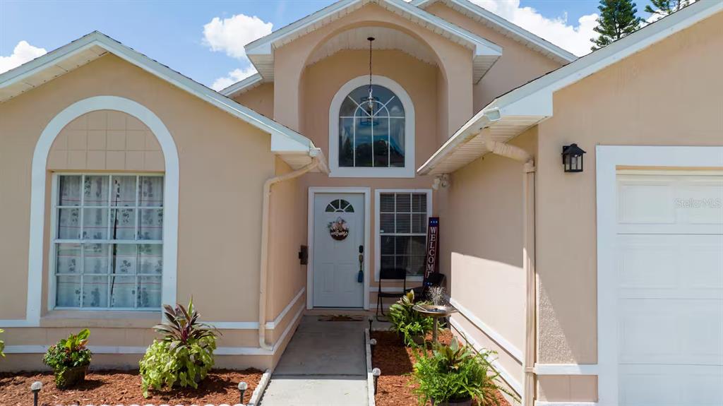 The exterior of a beige house features a white front door and an arched window — 751 COUNTRY WOODS CIRCLE, KISSIMMEE, FL