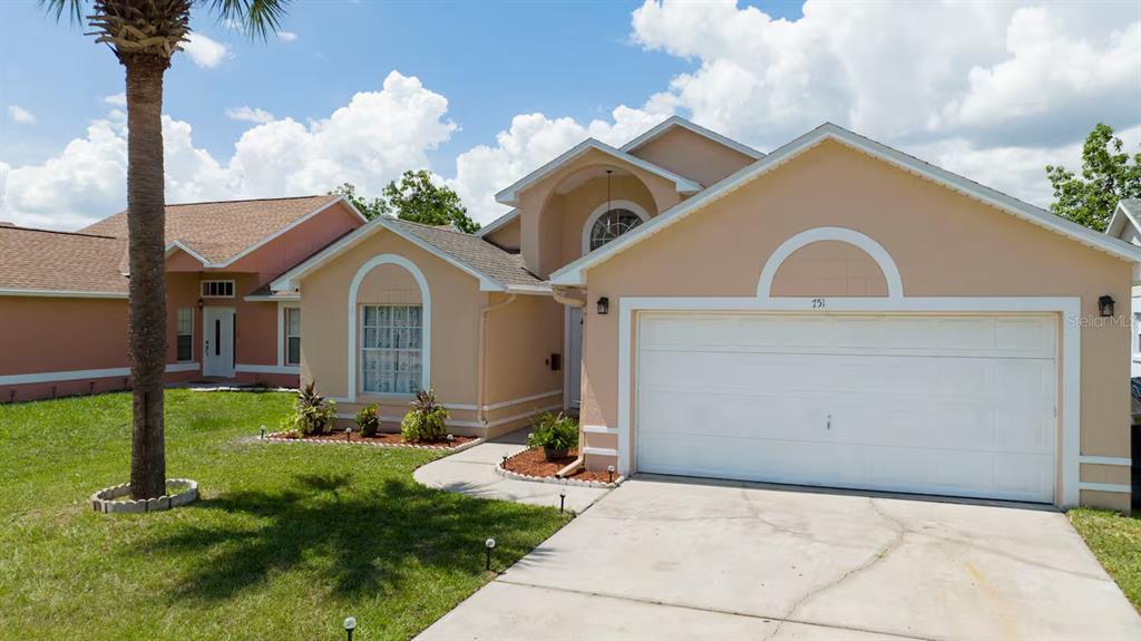 A single-story tan house with a two-car garage and a palm tree in the yard — 751 COUNTRY WOODS CIRCLE, KISSIMMEE, FL
