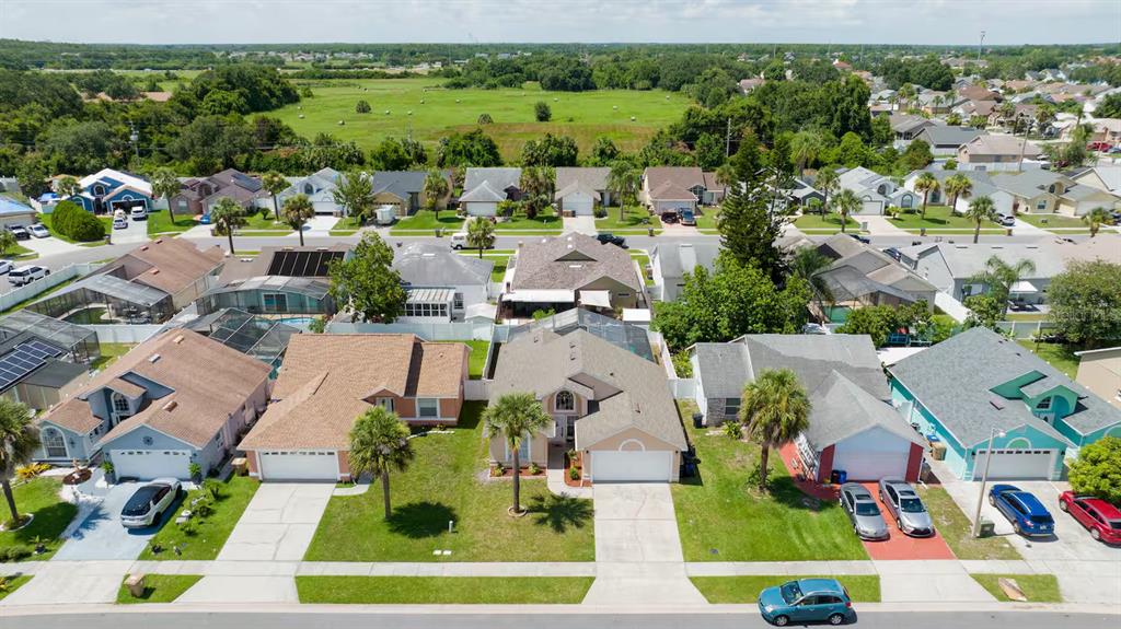 An aerial view shows a suburban street with several single-family homes and a grassy field — 751 COUNTRY WOODS CIRCLE, KISSIMMEE, FL