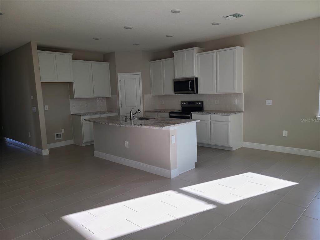A modern kitchen features white cabinets, granite countertops, a center island, and light tile flooring — 17758 CANTARINA COVE, LAKEWOOD RANCH, FL