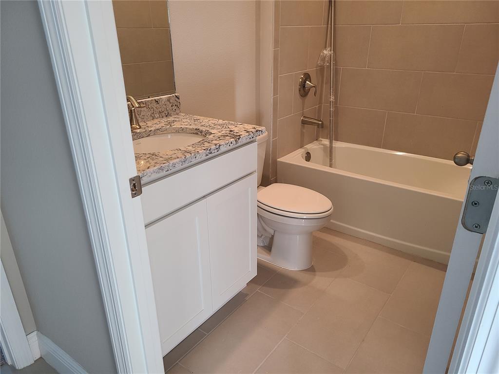 A bathroom features a white vanity with a granite countertop, a toilet, and a tub — 17758 CANTARINA COVE, LAKEWOOD RANCH, FL