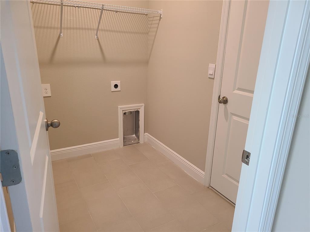 A laundry room features tile flooring, a wire shelf, and utility hookups on the wall — 17758 CANTARINA COVE, LAKEWOOD RANCH, FL