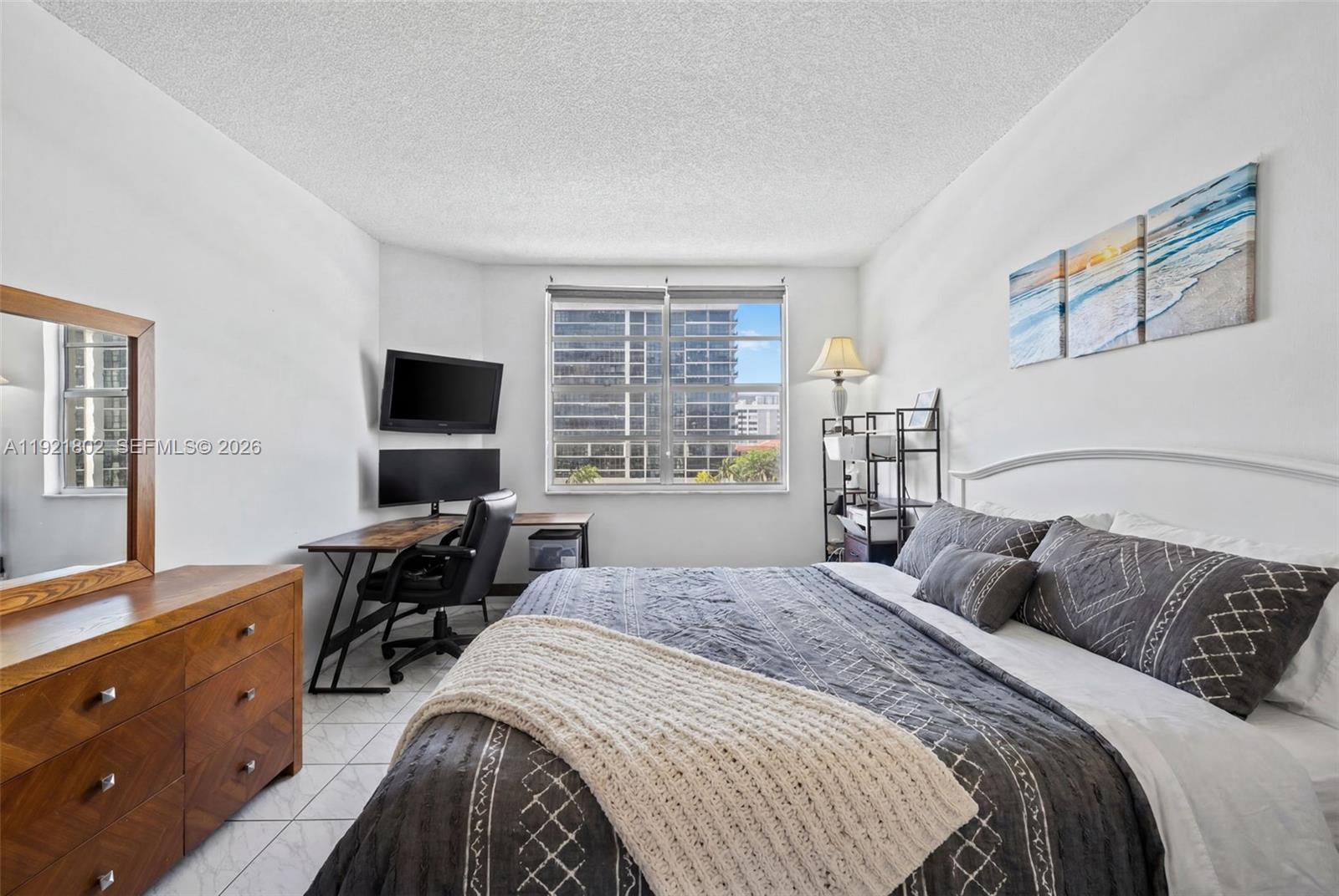 A bedroom features a bed with gray bedding, a desk with monitors, and a dresser — 1985 S Ocean Dr # 3A, Hallandale Beach FL 33009, HALLANDALE BEACH, FL