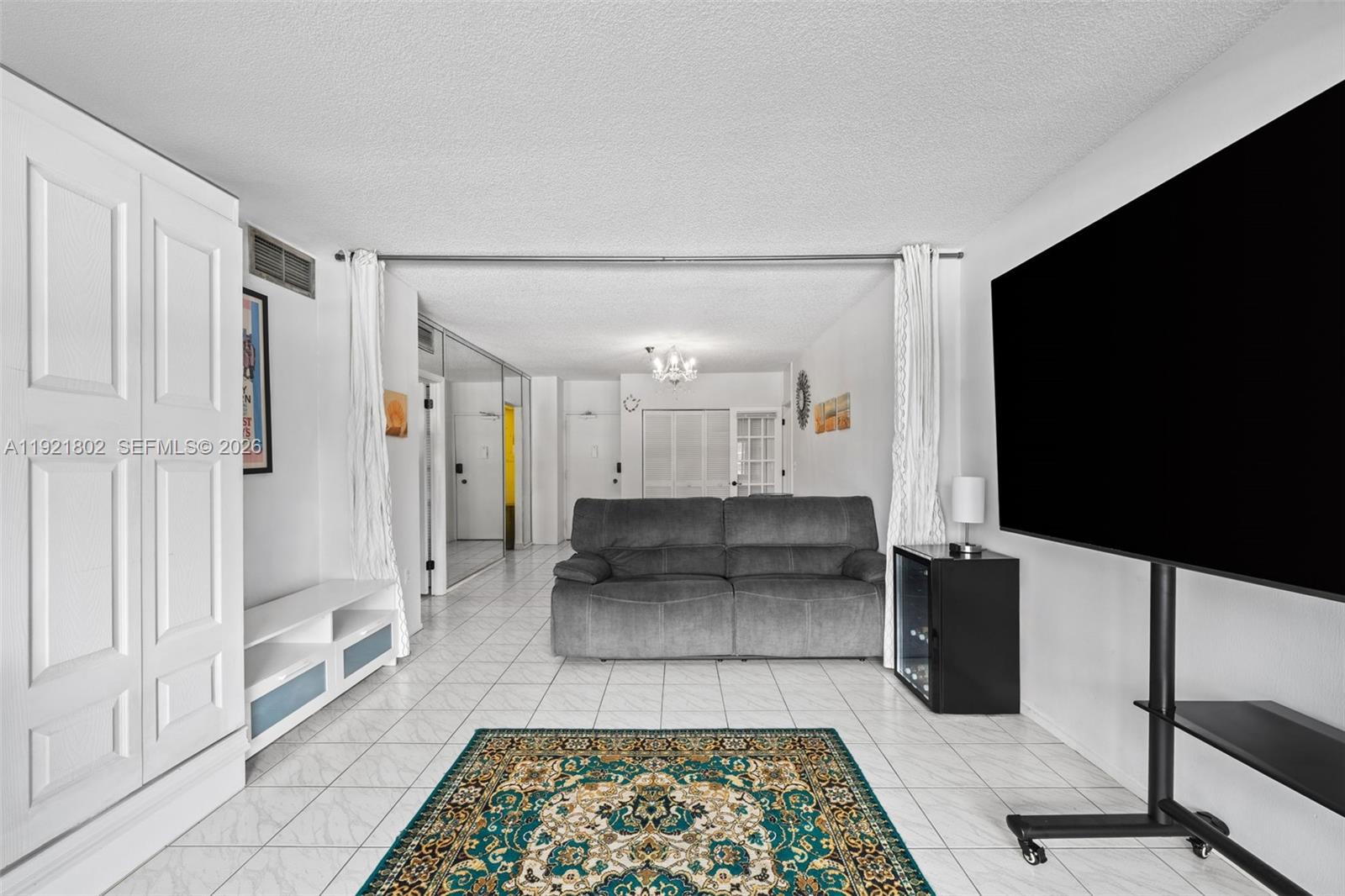 This living room features white tile flooring, a gray sofa, and a large television — 1985 S Ocean Dr # 3A, Hallandale Beach FL 33009, HALLANDALE BEACH, FL
